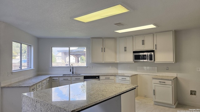 kitchen with white cabinets, sink, a kitchen island, light stone counters, and stainless steel appliances