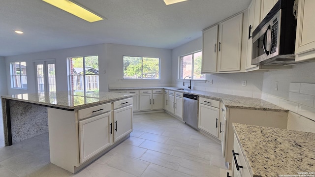 kitchen featuring appliances with stainless steel finishes, light stone counters, sink, a center island, and white cabinetry