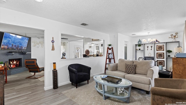 living room featuring hardwood / wood-style flooring, ceiling fan, a textured ceiling, and a brick fireplace