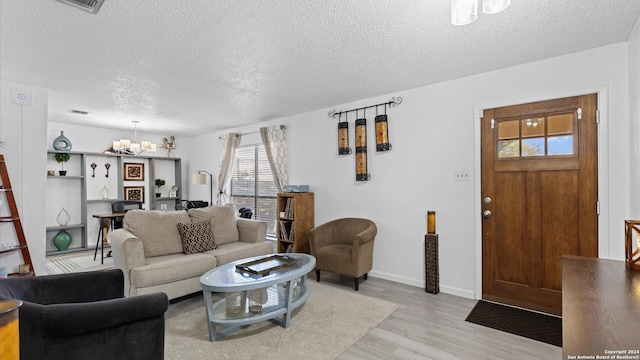 living area with a notable chandelier, visible vents, a textured ceiling, light wood-type flooring, and baseboards