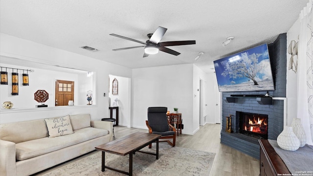 living room featuring a textured ceiling, light hardwood / wood-style flooring, a brick fireplace, and ceiling fan