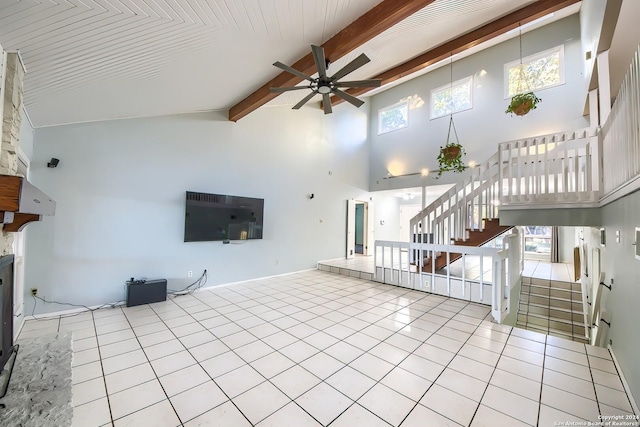 unfurnished living room with ceiling fan, light tile patterned floors, beamed ceiling, and a high ceiling