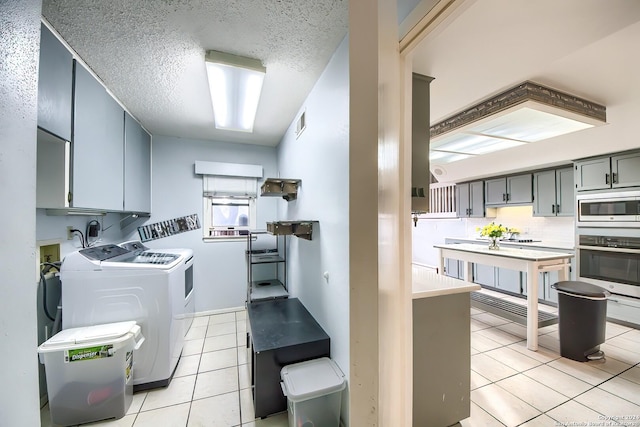 washroom featuring washer and dryer, light tile patterned flooring, cabinets, and a textured ceiling