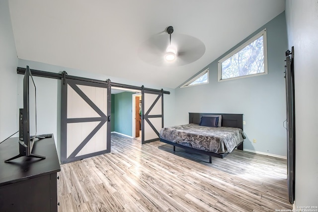 bedroom with a barn door, ceiling fan, light hardwood / wood-style flooring, and vaulted ceiling