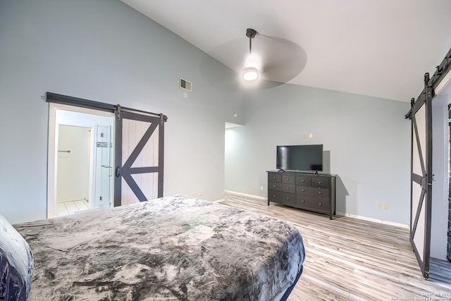 bedroom featuring ceiling fan, a barn door, high vaulted ceiling, light hardwood / wood-style flooring, and connected bathroom