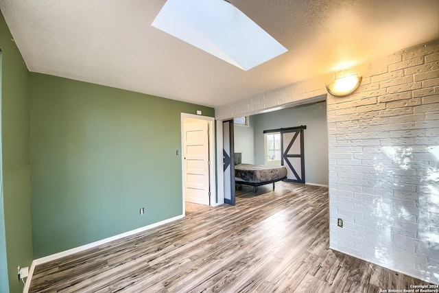 interior space featuring wood-type flooring, a barn door, and a skylight