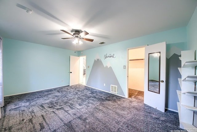 unfurnished bedroom featuring a walk in closet, carpet floors, and ceiling fan