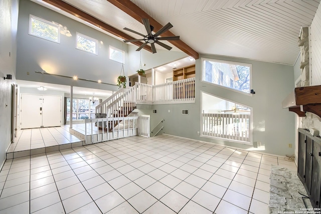 unfurnished living room with ceiling fan with notable chandelier, light tile patterned floors, high vaulted ceiling, beamed ceiling, and plenty of natural light