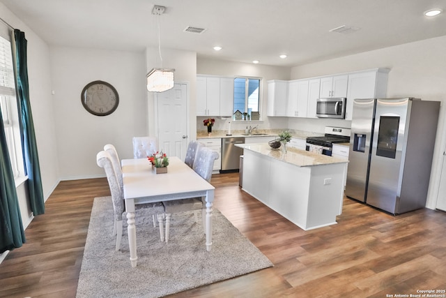 kitchen with a kitchen island, white cabinetry, stainless steel appliances, and hanging light fixtures