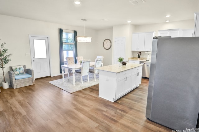 kitchen with hanging light fixtures, stainless steel appliances, a kitchen island, white cabinets, and hardwood / wood-style flooring