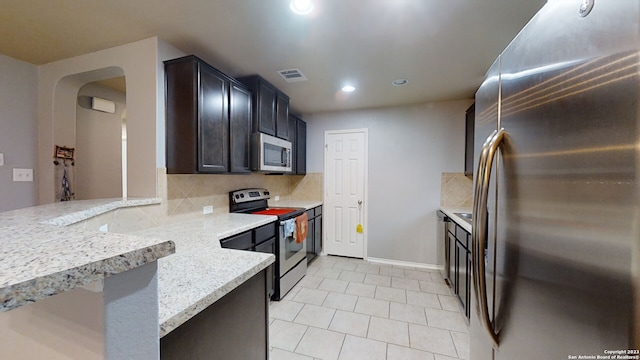 kitchen with light tile patterned floors, stainless steel appliances, light stone counters, and tasteful backsplash