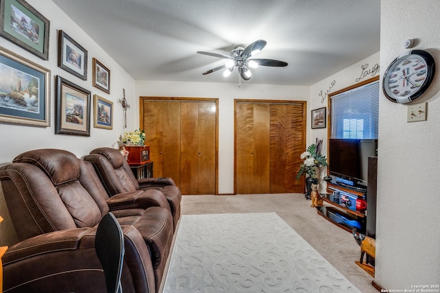 living room featuring ceiling fan, light colored carpet, and a textured ceiling