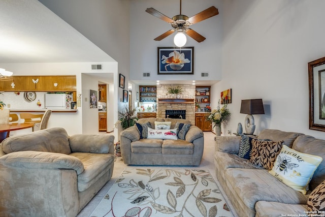 living room with built in shelves, ceiling fan, a fireplace, and a high ceiling