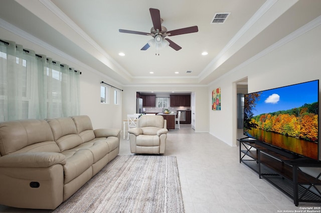 living room with ceiling fan, a raised ceiling, and ornamental molding