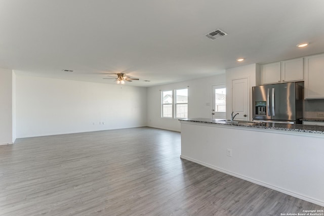 kitchen with stainless steel fridge, dark stone counters, ceiling fan, light hardwood / wood-style flooring, and white cabinetry