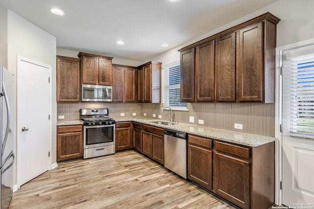 kitchen featuring sink, a healthy amount of sunlight, light stone counters, light hardwood / wood-style flooring, and appliances with stainless steel finishes