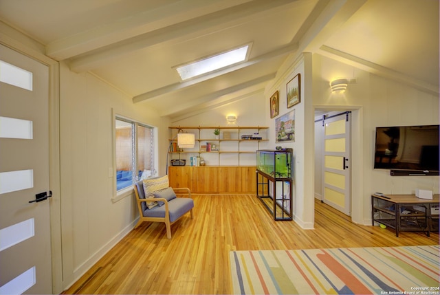 sitting room with a barn door, lofted ceiling with skylight, a wealth of natural light, and light hardwood / wood-style flooring