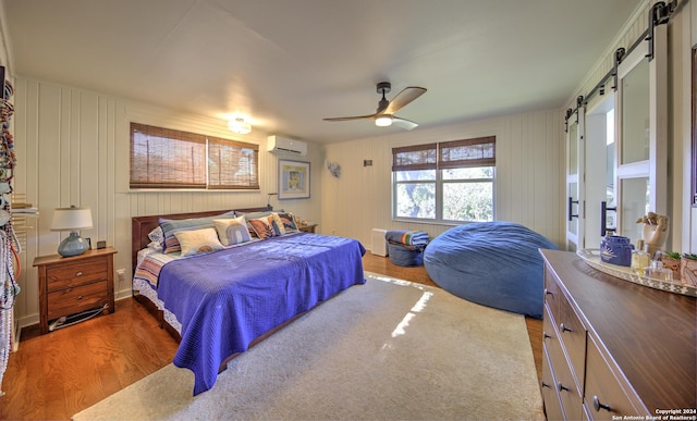 bedroom featuring a wall unit AC, ceiling fan, a barn door, and wood-type flooring