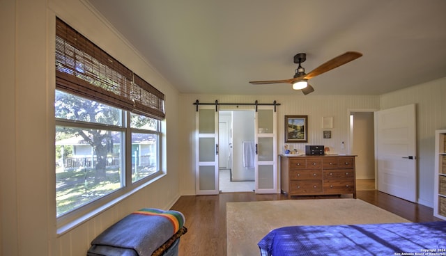 bedroom featuring hardwood / wood-style floors, ornamental molding, ceiling fan, and a barn door