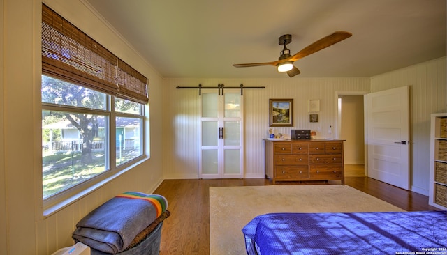 bedroom with ceiling fan, crown molding, a barn door, and hardwood / wood-style flooring