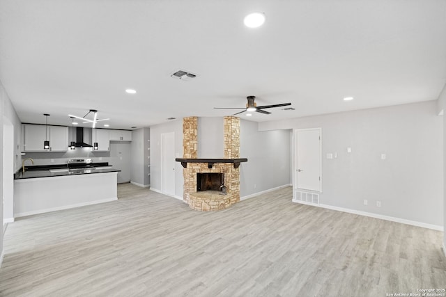 unfurnished living room featuring ceiling fan, light hardwood / wood-style floors, sink, and a fireplace