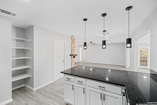 kitchen featuring white cabinetry, ceiling fan, dark stone counters, decorative light fixtures, and light wood-type flooring