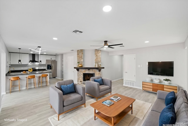 living room featuring ceiling fan, light hardwood / wood-style floors, a stone fireplace, and sink