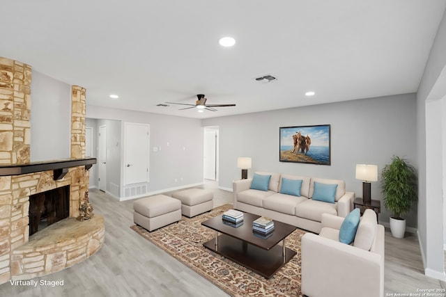 living room featuring ceiling fan, a stone fireplace, and light hardwood / wood-style flooring