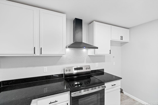 kitchen featuring stainless steel range with electric cooktop, dark stone counters, white cabinets, wall chimney range hood, and light hardwood / wood-style flooring