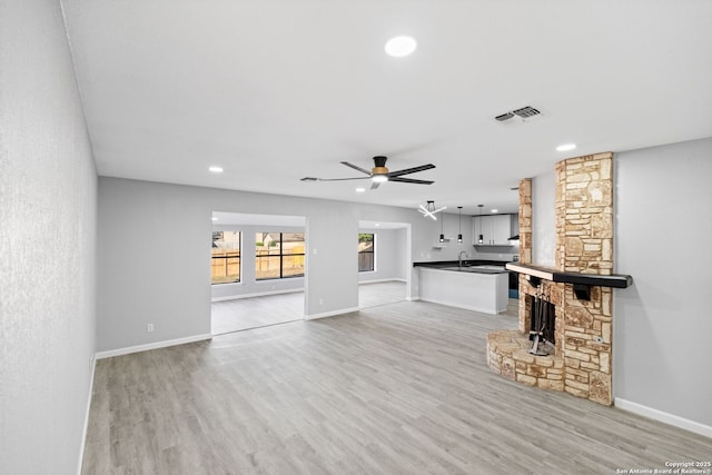 unfurnished living room featuring a stone fireplace, ceiling fan, sink, and light hardwood / wood-style floors