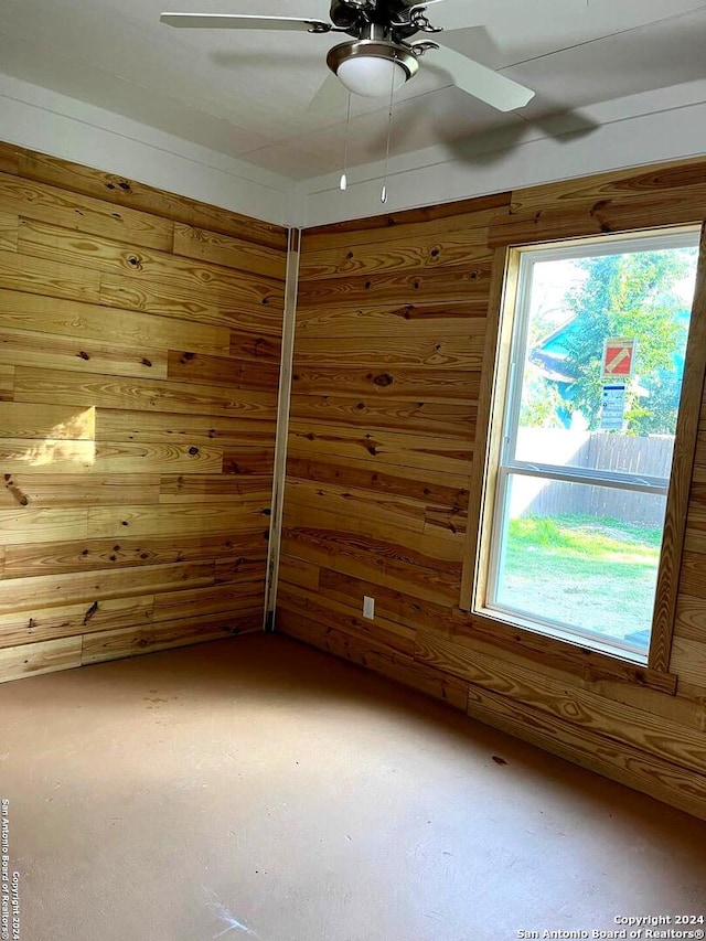 empty room featuring concrete flooring, ceiling fan, and wood walls