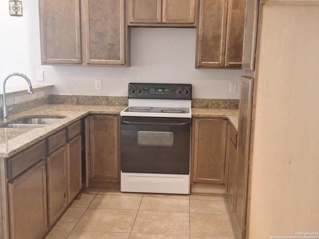 kitchen with light tile patterned flooring, light stone counters, white electric stove, and sink