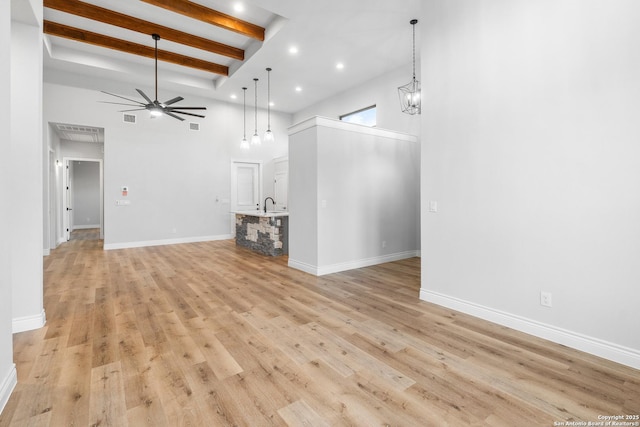 unfurnished living room with a towering ceiling, ceiling fan, sink, beam ceiling, and light hardwood / wood-style floors