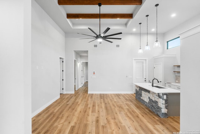 unfurnished living room with ceiling fan, sink, beamed ceiling, a towering ceiling, and light wood-type flooring