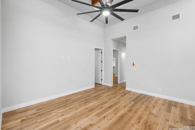 spare room with ceiling fan, light wood-type flooring, and a towering ceiling