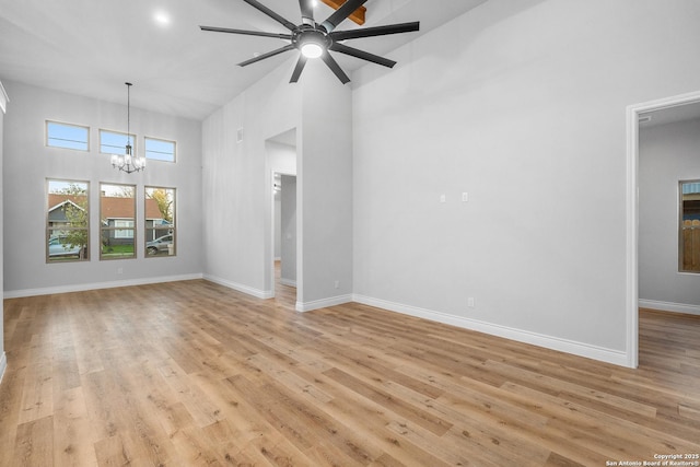 unfurnished living room featuring light wood-type flooring, a high ceiling, and ceiling fan with notable chandelier