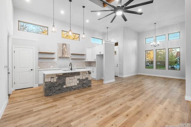 kitchen with a center island with sink, decorative light fixtures, white cabinetry, and wall chimney range hood