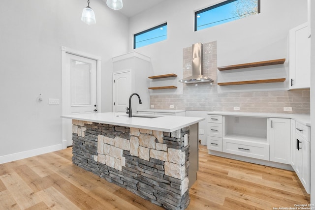 kitchen with white cabinetry, sink, wall chimney exhaust hood, backsplash, and pendant lighting