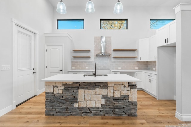 kitchen featuring pendant lighting, a kitchen island with sink, wall chimney exhaust hood, and sink