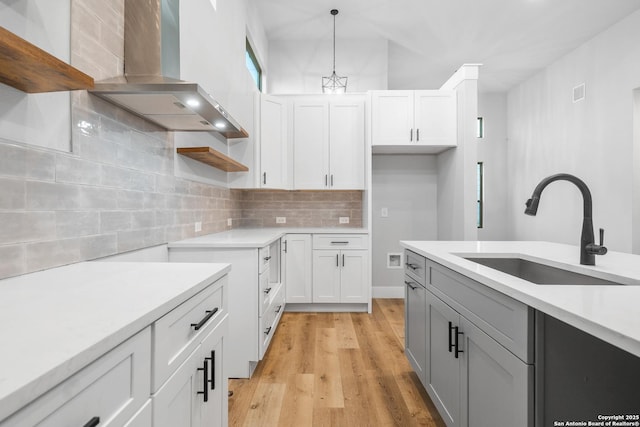 kitchen featuring pendant lighting, white cabinets, wall chimney range hood, sink, and light wood-type flooring