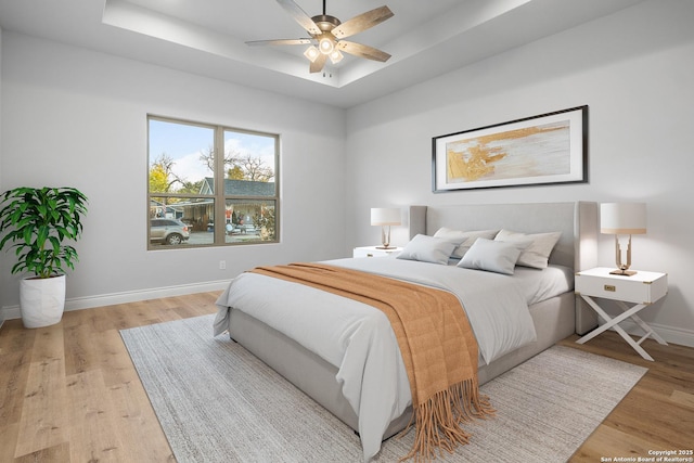 bedroom with a tray ceiling, light hardwood / wood-style flooring, and ceiling fan