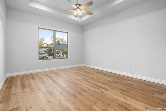 spare room with a raised ceiling, ceiling fan, and light hardwood / wood-style floors