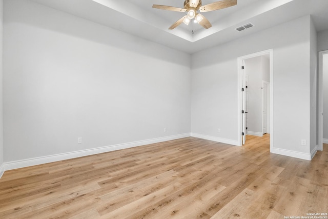 empty room with light hardwood / wood-style floors, a raised ceiling, and ceiling fan