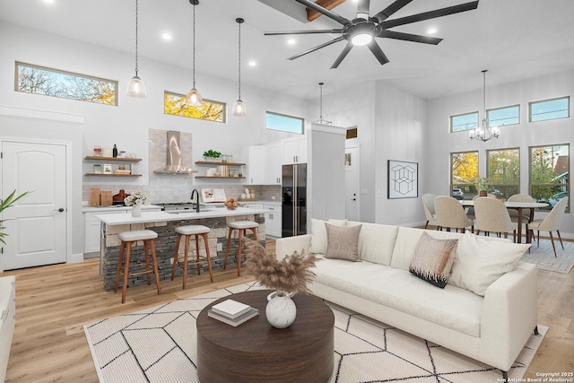 living room featuring ceiling fan with notable chandelier, light hardwood / wood-style floors, and a high ceiling