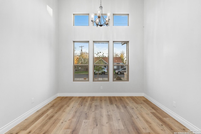 spare room featuring a towering ceiling, light hardwood / wood-style flooring, and an inviting chandelier