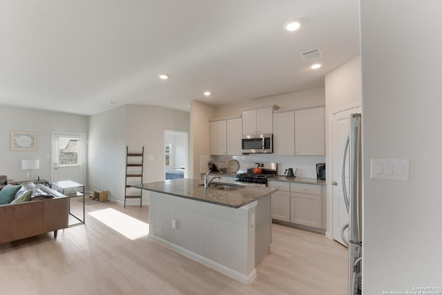 kitchen with white cabinets, light hardwood / wood-style floors, an island with sink, and appliances with stainless steel finishes