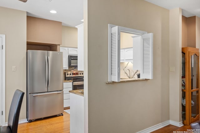 kitchen with backsplash, stainless steel appliances, white cabinetry, and light hardwood / wood-style flooring