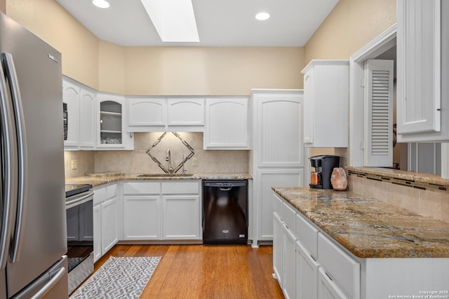 kitchen with black appliances, white cabinets, sink, a skylight, and light stone countertops