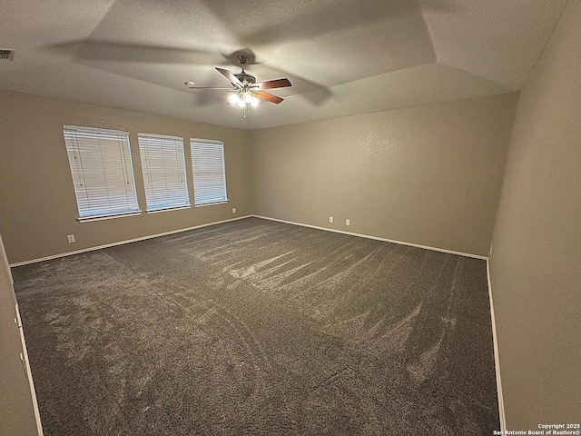 empty room with dark colored carpet, a raised ceiling, and ceiling fan