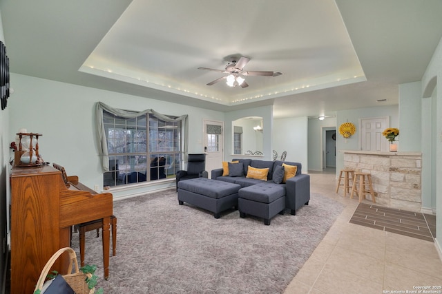 living room with a raised ceiling, ceiling fan, and light tile patterned floors